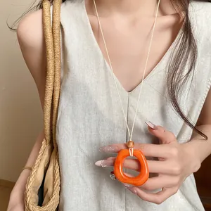 Detailed close-up of orange resin geometric ring necklace on white cord with linen top