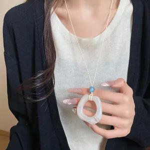 Detail of minimalist resin ring necklace worn on a white top and black cardigan.