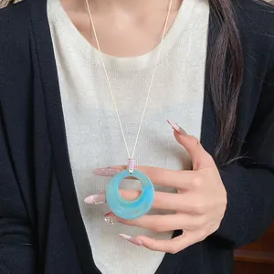 Detail of blue resin ring pendant necklace on model's hand for stylish sweater accessory