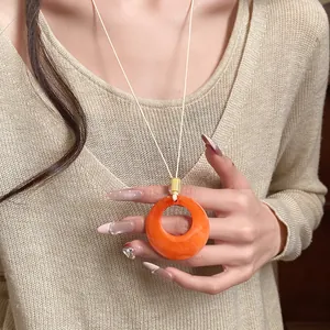 Close-up of a minimalist orange resin circle pendant necklace on a beige sweater