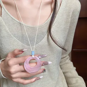 Detail shot of a minimalist pink resin ring pendant necklace on a long white cord