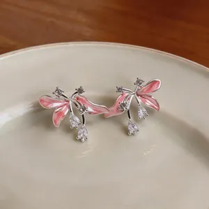 Gros plan de boucles d'oreilles fleur en émail rose avec zircone sur une assiette.