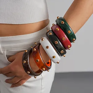 Close-up of stacked retro resin bangles with marbled patterns and gold rivet studs