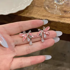 Détail de boucles d'oreilles fleurs en émail rose avec zircons brillants sur une main