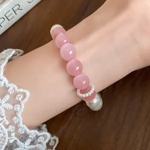 Detail view of pink cat's eye and pearl beaded bracelet with small pearl charm on wrist