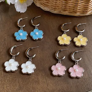 Detailed macro view of colorful resin flower earrings with pearl centers on wooden surface
