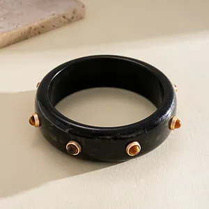 Detail view of a retro black resin bangle with marbled texture and gold rivets.