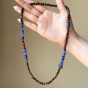 Detail view of a vintage wooden and blue stone beaded necklace held in hand.