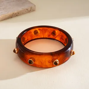 Close-up of vintage resin bangle featuring amber tortoiseshell pattern and gold rivets