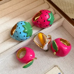 Detailed view of colorful enamel strawberry and fruit rings in a beige jewelry display