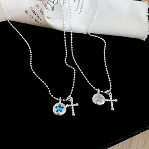 Detailed view of silver ball chain necklace with blue star and beaded cross pendants