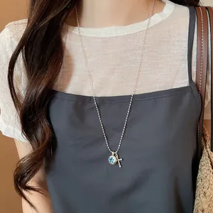 Detailed shot of a silver ball chain necklace with star and cross pendants on a model