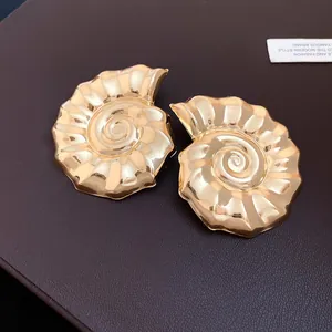 Dettaglio degli orecchini vintage a forma di conchiglia dorata su superficie in pelle