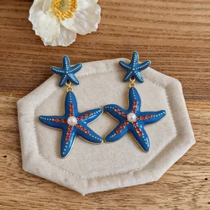Dettaglio di orecchini a stella marina blu con strass rossi e perla centrale incastonata.