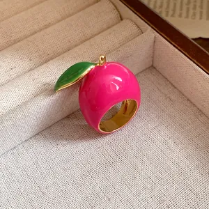Detail shot of a sweet pink strawberry enamel ring with a green leaf and gold band.