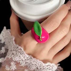 Close-up detail of a cute pink strawberry enamel ring with a green leaf worn on a hand.