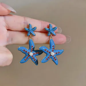 Primo piano di orecchini a stella marina in smalto blu con strass rossi e perle