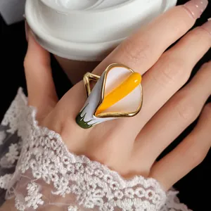 Close-up of elegant white and yellow enamel Calla Lily ring on finger with lace sleeve.
