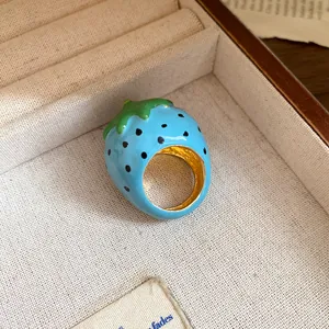 Macro view showing the vibrant blue enamel texture of a cute strawberry-shaped ring