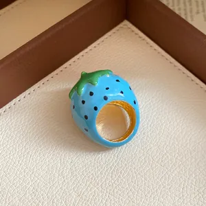 Close-up of a vibrant blue strawberry enamel ring with golden interior finish.