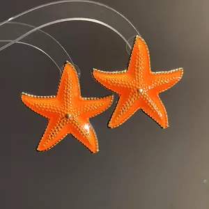 Close-up of bright orange enamel starfish stud earrings with gold trim for summer.