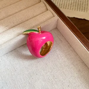 Close-up detail of a glossy pink enamel apple-shaped ring with a small green leaf