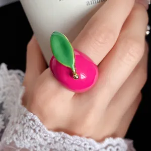 Close-up of a vibrant pink enamel fruit ring with a green leaf detail worn on a finger.