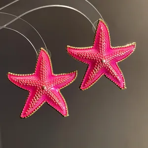 Macro view of vibrant fuchsia pink starfish earrings with gold-toned beaded edges
