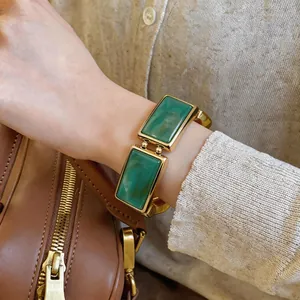 Detailopname van vintage armband met groene rechthoekige harschakels en gouden montuur