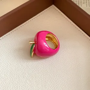 Macro view of a vibrant pink enamel strawberry ring with gold accents and green leaf detail