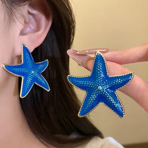 Macro view of large blue enamel starfish stud earrings featuring gold beaded edges.