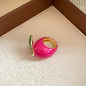 Close-up of a vibrant pink strawberry enamel ring with green leaf and gold plating.