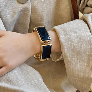 Detailopname van een retro rechthoekige armband met gouden montuur en donkerblauwe hars.