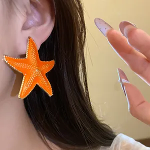 Close-up of a vibrant orange starfish earring with gold trim worn on a female ear.