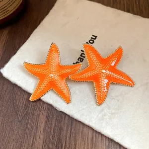 Close-up view of bright orange starfish stud earrings with a glossy drip oil finish.
