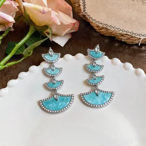Macro view of tiered fan-shaped earrings with zircon pavé borders and turquoise enamel