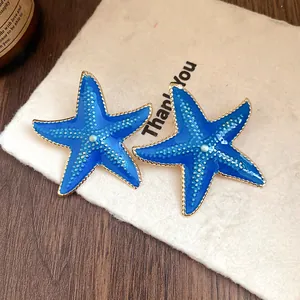 Close-up detail of summer vacation style blue oil-dripped starfish earrings with gold trim.