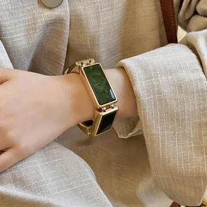 Gedetailleerde close-up van een gouden rechthoekige schakelarmband met groene marmeren inleg