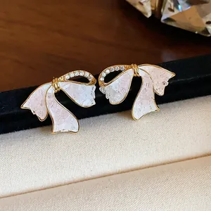 Nahaufnahme eleganter 18k vergoldeter Schleifenohrringe mit Zirkonia-Inlay und Marmortextur