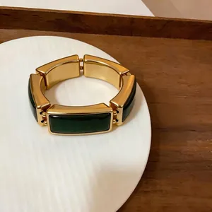 Detail van een vintage goudkleurige armband met groene rechthoekige segmenten op een bord.