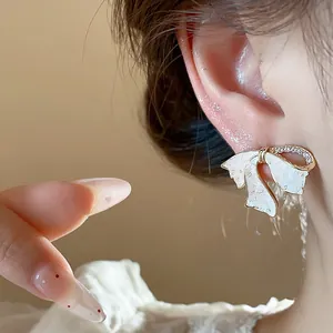 Nahaufnahme eines vergoldeten Schleifenohrrings mit Zirkonia und weißem Emaille-Finish