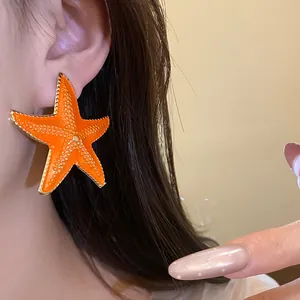 Detailed close-up of bright orange starfish earring with gold border worn by a model.
