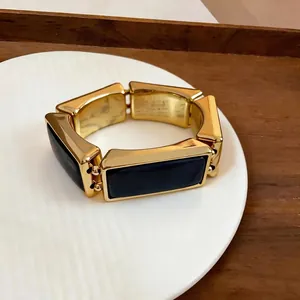 Detailopname van een vintage gouden en zwart emaille rechthoekige armband op een bord