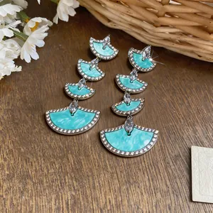 Detail view of 18k gold plated fan-shaped earrings with teal enamel and zircons.