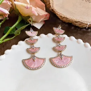 Close-up of elegant 18k gold plated fan-shaped earrings with pink stones on a plate