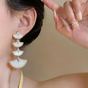 Detail of 18k gold plated fan-shaped drop earrings with pavé zircons on model ear