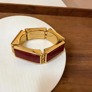 Detailopname van een gouden schakelarmband met rechthoekige, bordeauxrode harssegmenten.