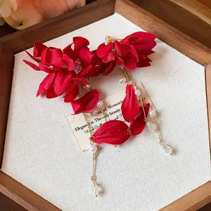 Macro detail showing the red fabric flower petals, long gold tassels, and white pearls on earrings