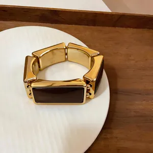 Detailweergave van een vintage goud en bruine rechthoekige schakelarmband op een bord.