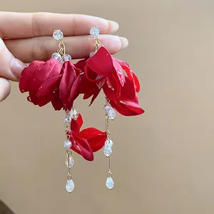 Close-up of red fabric flower earrings with elegant crystal and pearl tassels.
